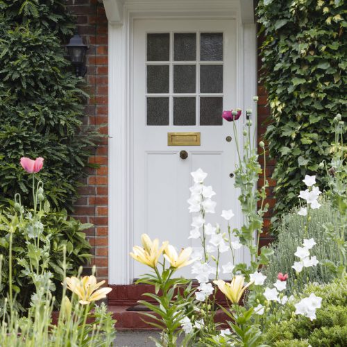 Half-glazed wooden front door of a period house in London with an attractive flower garden