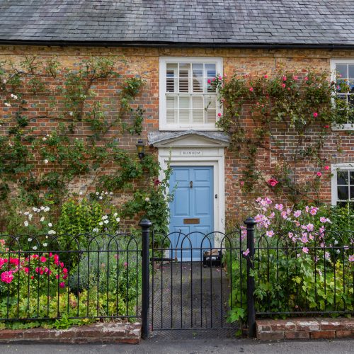 The exterior of an english cottage with flowers blooming in the front garden and sash windows, A typical english countryside cottage